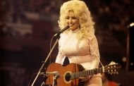 Dolly Parton performs with a guitar, 1976. (Image via Getty)